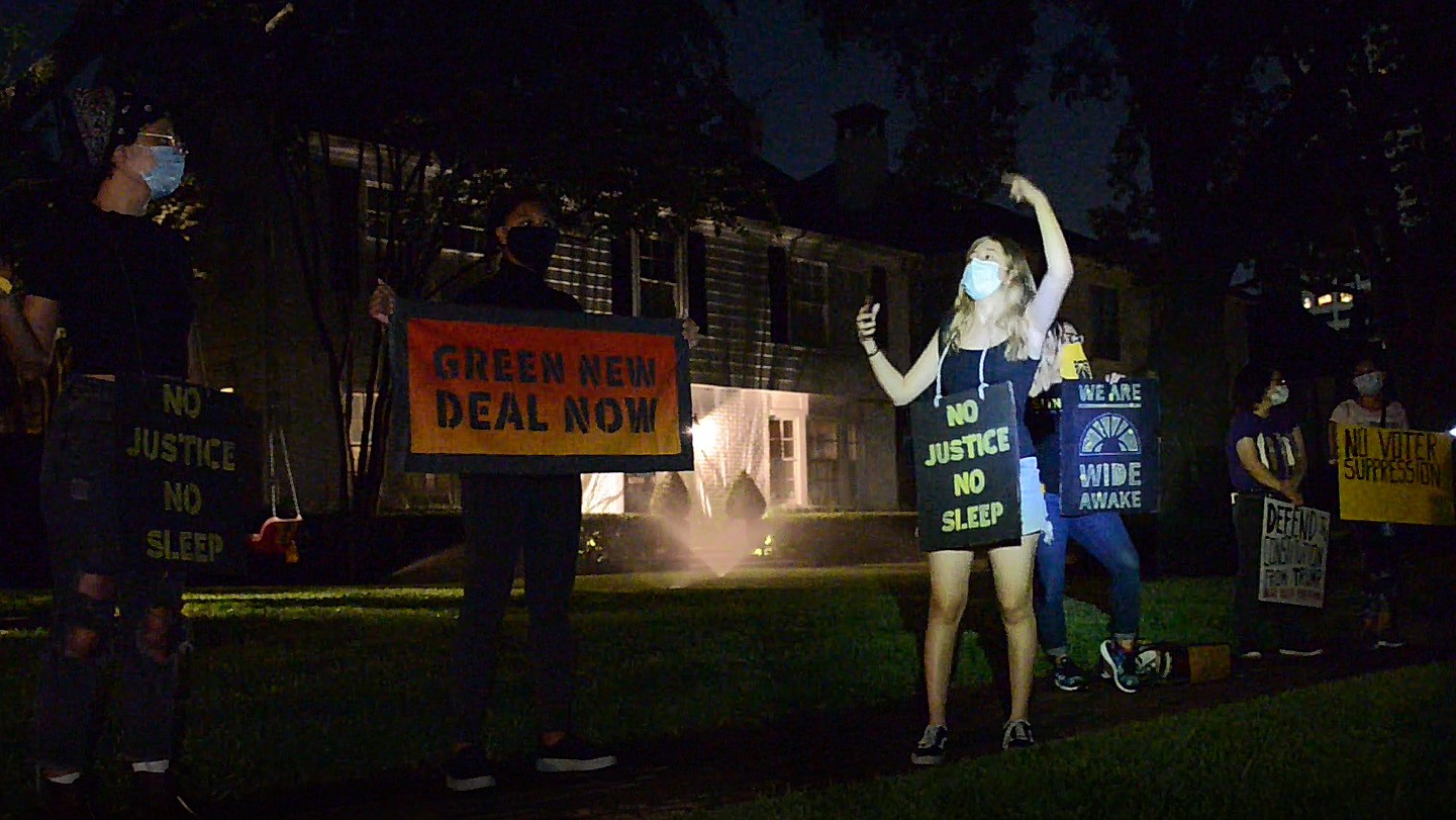 Young people protesting in night with signs saying "No justice, no sleep" and "Green New Deal Now"